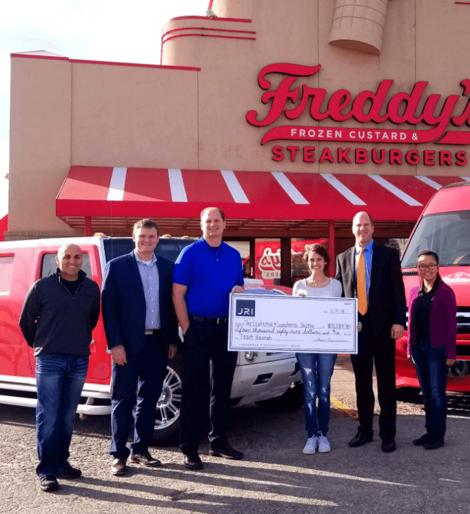Six people in front of a Freddy's with a check from JRI