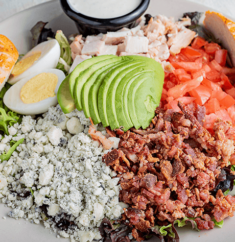 A close up of a cobb salad with egg, cheese, bacon, avocado, ham and tomato.