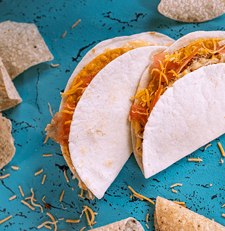 Two soft tacos leaning on one another on a blue background